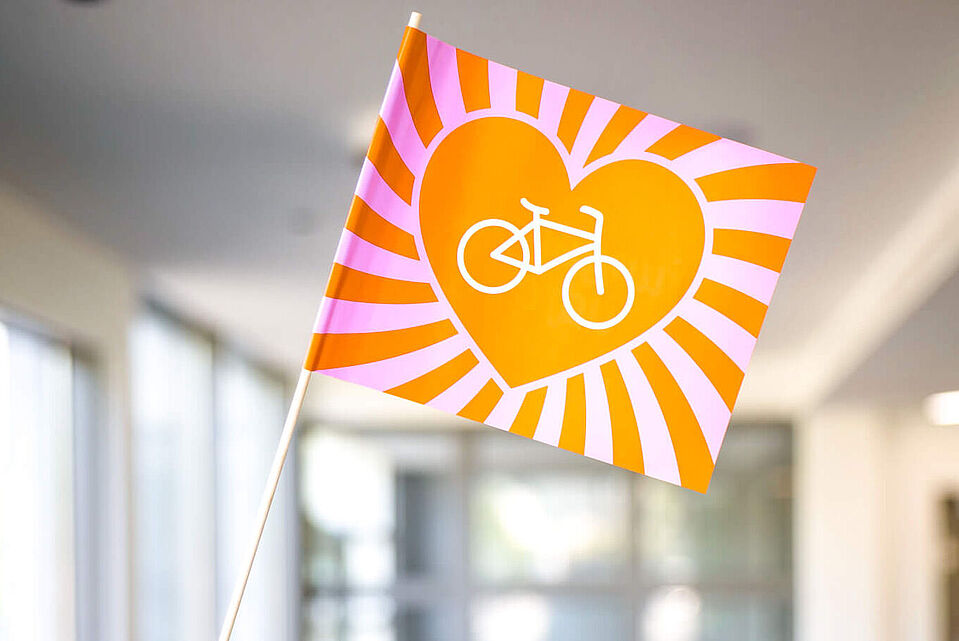 Junger ADFC Eine kleine Fahne mit Herz und Fahrrad steht vor einer Gruppe im Raum.